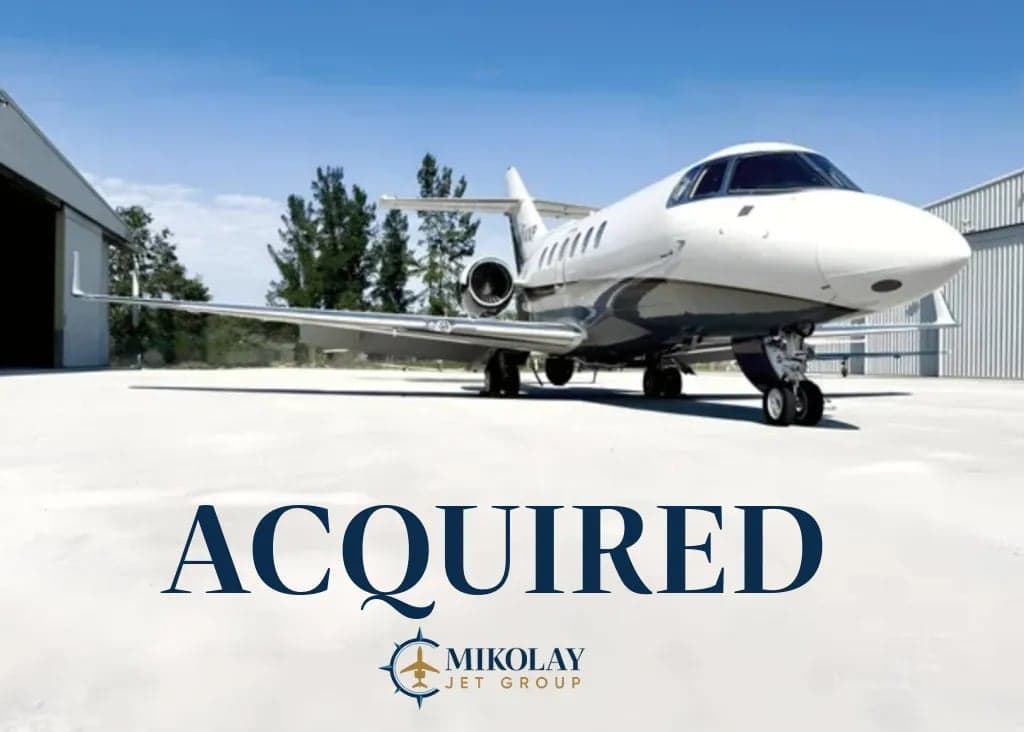 A white jet aircraft is parked on the tarmac in front of a hangar, with the word "ACQUIRED" overlaid.