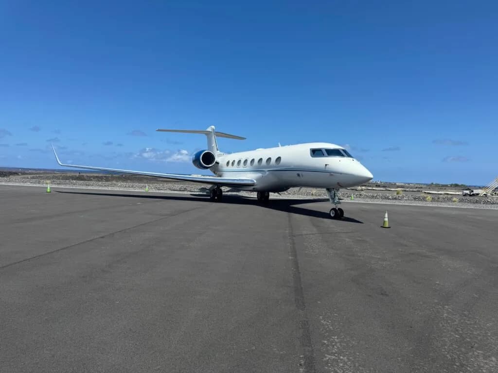 A white Gulfstream business jet with blue accents on the engine nacelles and tail, parked on an asphalt tarmac under a clear blue sky.
