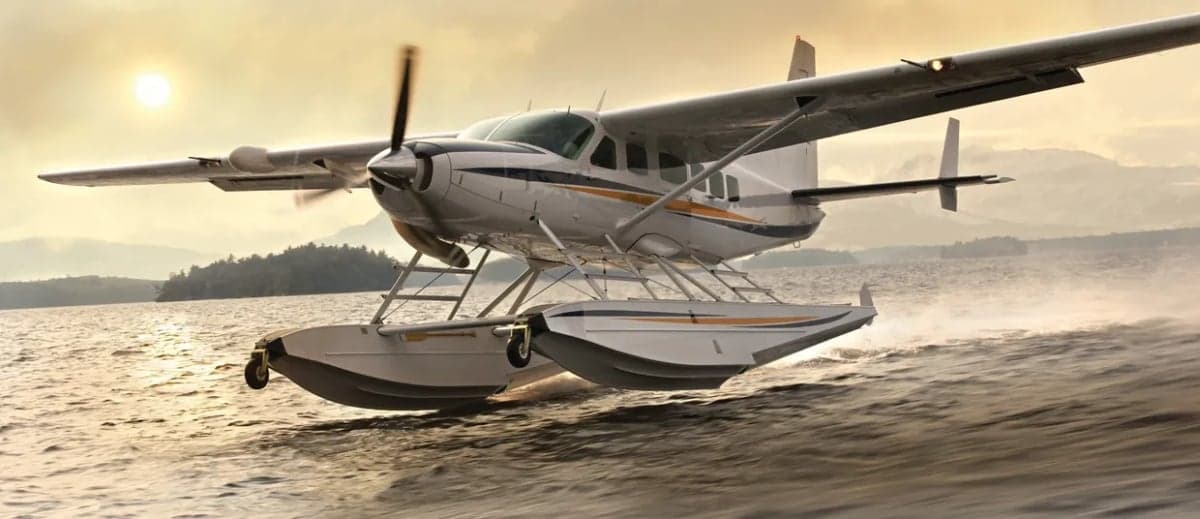 A Cessna Caravan seaplane takes off from the water at sunset.