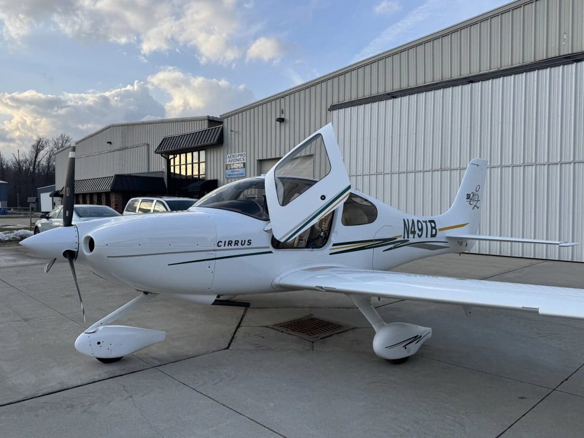 A Cirrus SR20 aircraft with open doors is parked outside a hangar.
