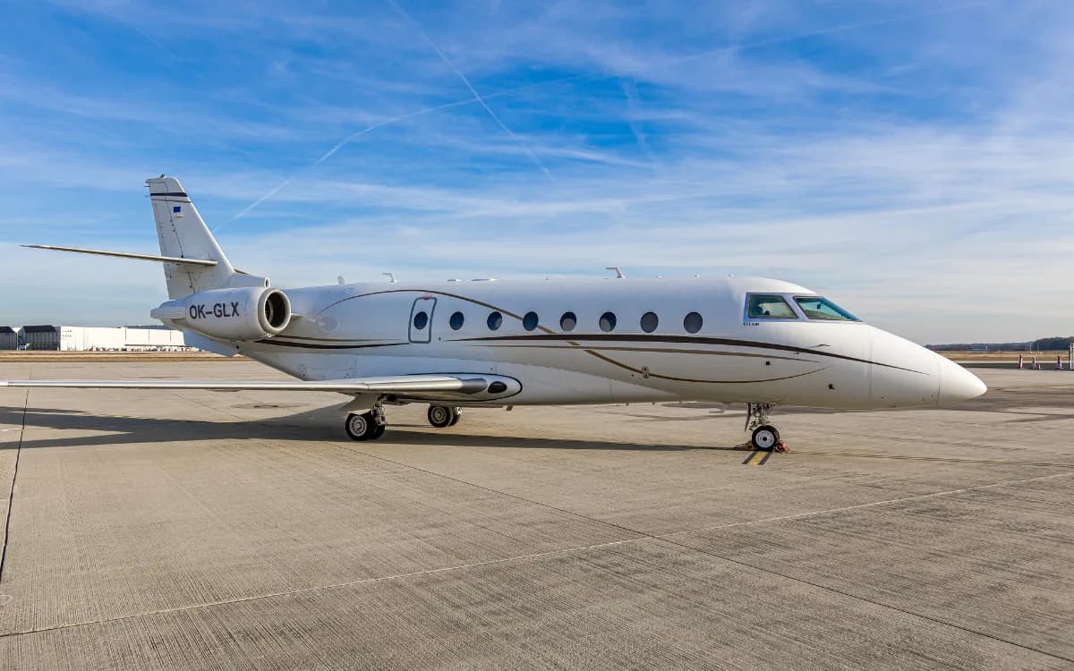 A white jet aircraft with brown and gold accents parked on the tarmac.