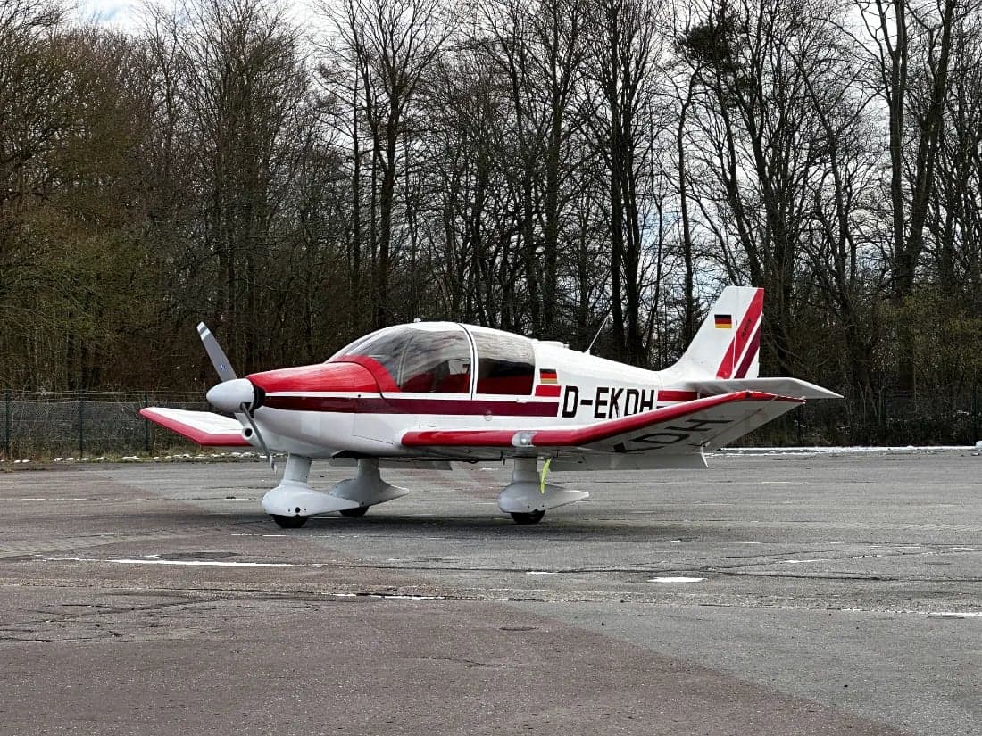Side view of a white and red aircraft with German flag on the tail, parked on the tarmac.