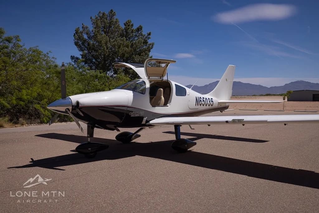 A white and black single-engine aircraft, N65035, with its gull-wing doors open, parked on an asphalt ramp under a clear blue sky.