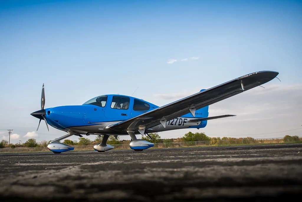 A blue and silver Cirrus SR22T GTS Carbon aircraft (N127DF) parked on a tarmac under a clear blue sky.