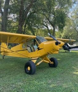 A yellow Cubcrafters aircraft is parked on the grass.