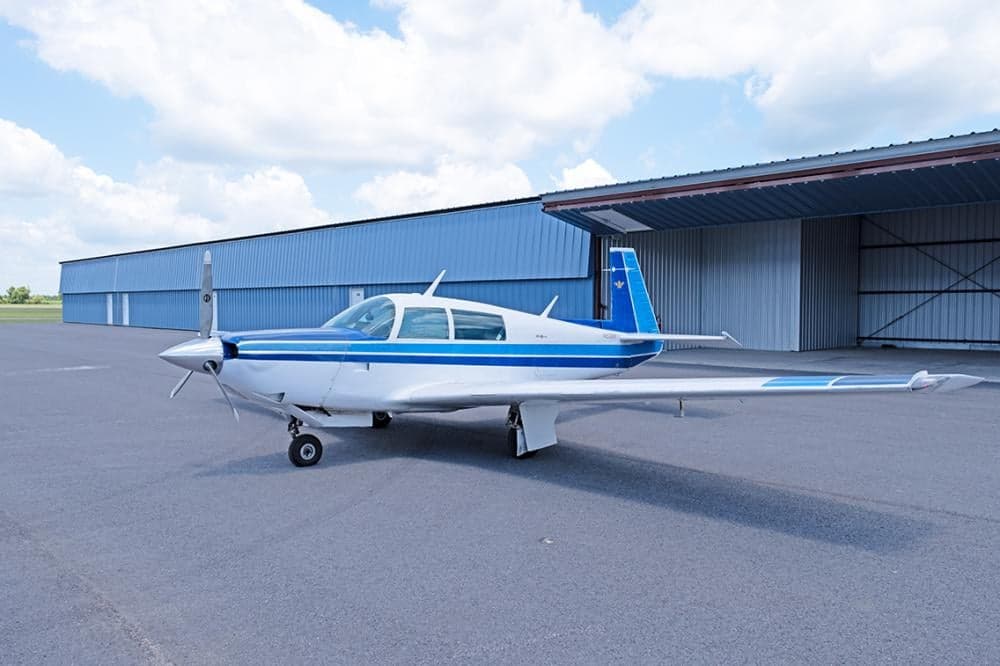 Side view of a white and blue Mooney M20F aircraft parked on the tarmac.
