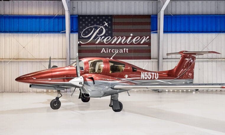 Diamond DA62 aircraft with red and gray paint scheme in a hangar.