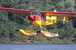 Yellow and red seaplane flying over water.
