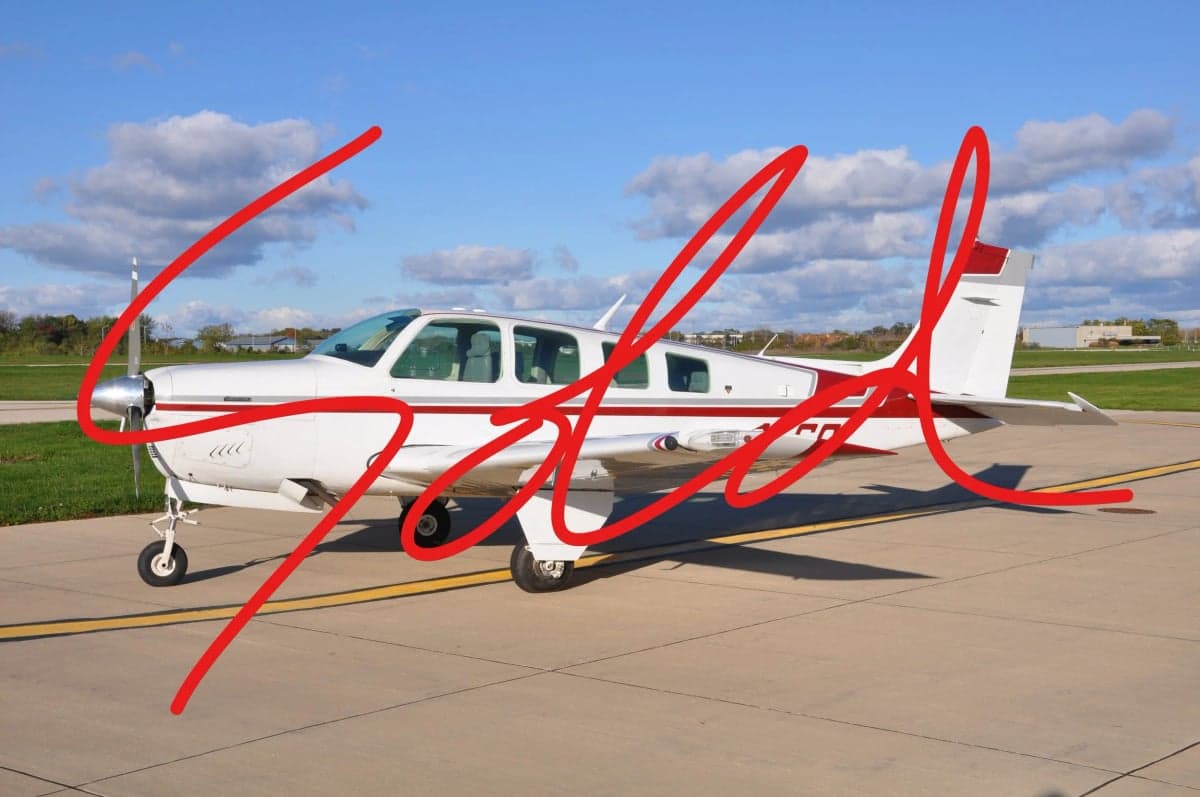 A Beechcraft Bonanza aircraft with a red and white paint scheme, parked on the tarmac with a SOLD overlay.