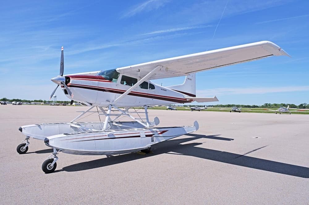A Cessna 206 on floats is parked on the tarmac on a sunny day.
