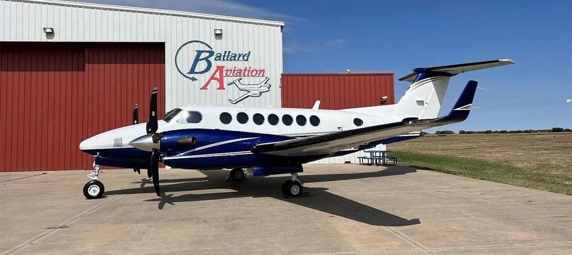 A Beechcraft King Air sits on the tarmac in front of a hangar.
