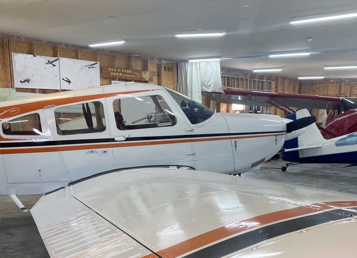 A white and orange aircraft is parked in a hangar, with a view of the wing and fuselage.