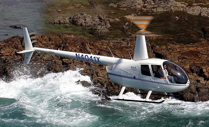Robinson R44 helicopter flying near the ocean.