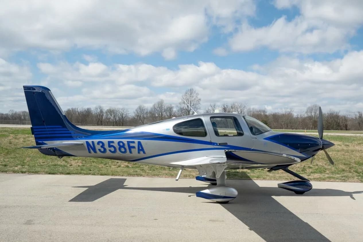 A silver and blue Cirrus SR22T aircraft, registration N358FA, parked on an airfield under a partly cloudy sky.