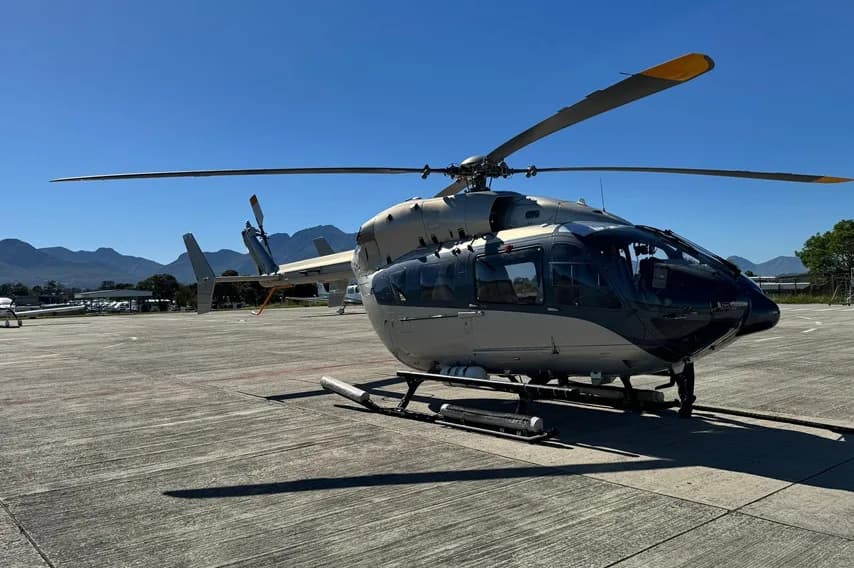 Helicopter parked on the tarmac with mountains in the background.