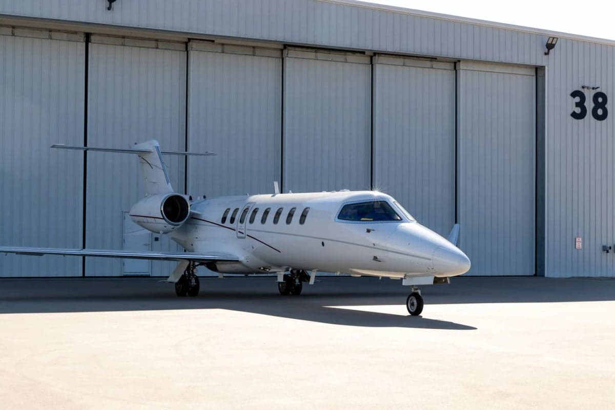 A white Learjet 45XR sits on the tarmac in front of a hangar.