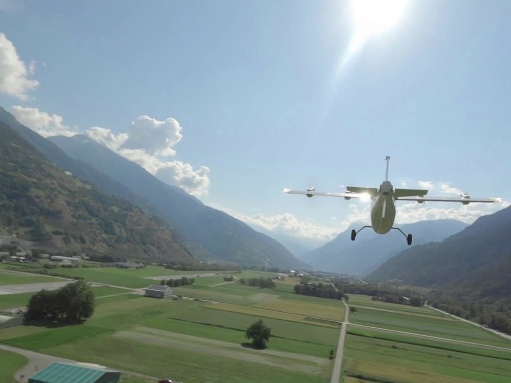 An aircraft flying over a valley with mountains in the background.