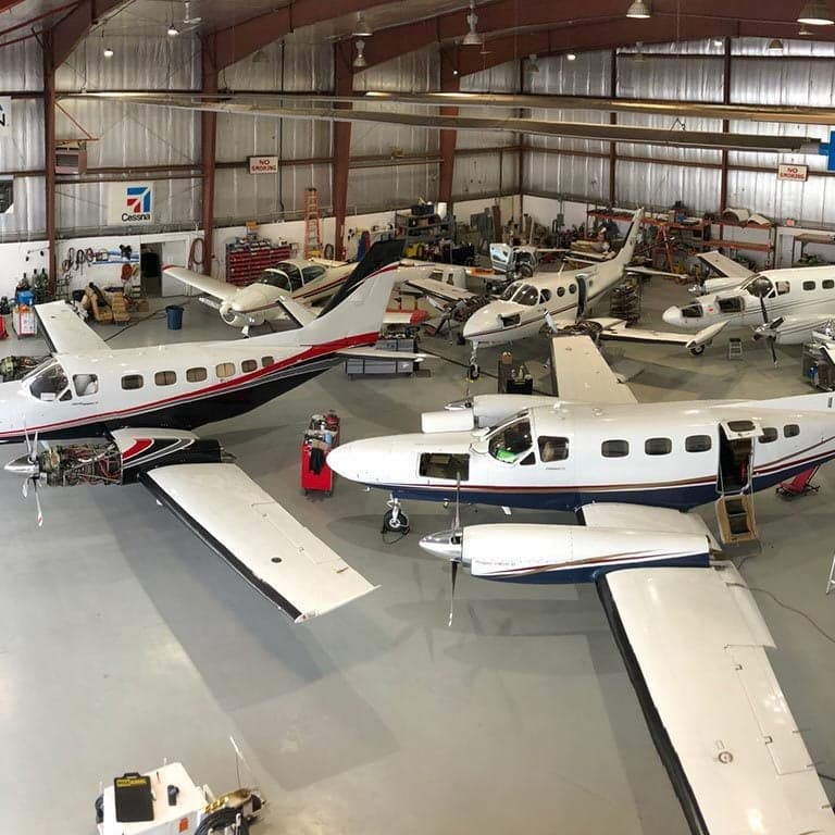 Overhead view of several Cessna aircraft inside a hangar, some undergoing maintenance.