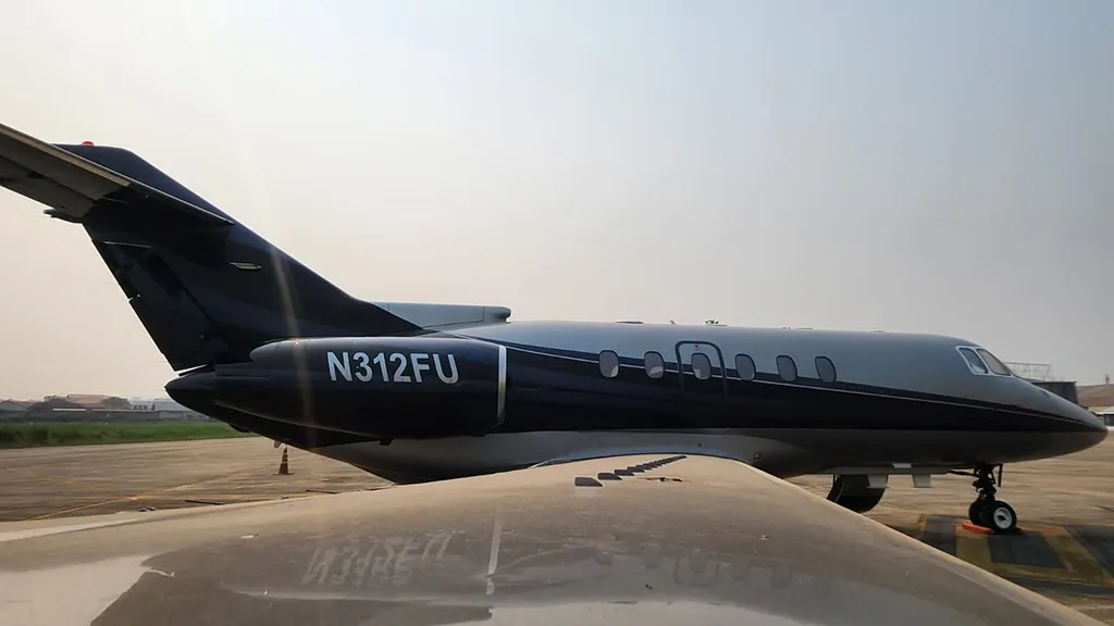 A side view of a dark blue and silver business jet with registration N312FU on the engine, parked on a tarmac.