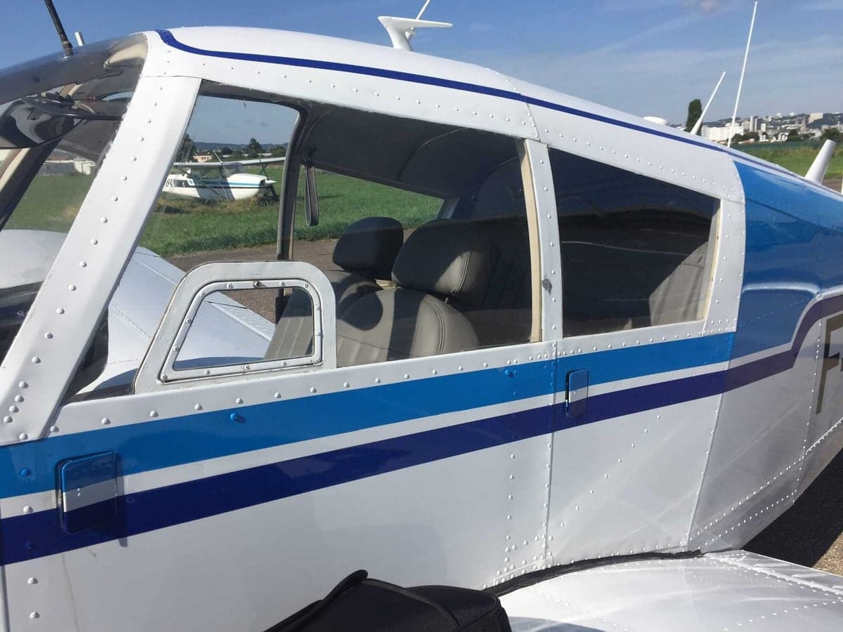 Close-up view of the white and blue fuselage and windows of a light aircraft on the ground.