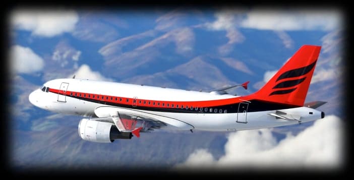 A white and red aircraft is flying in front of a mountain range.