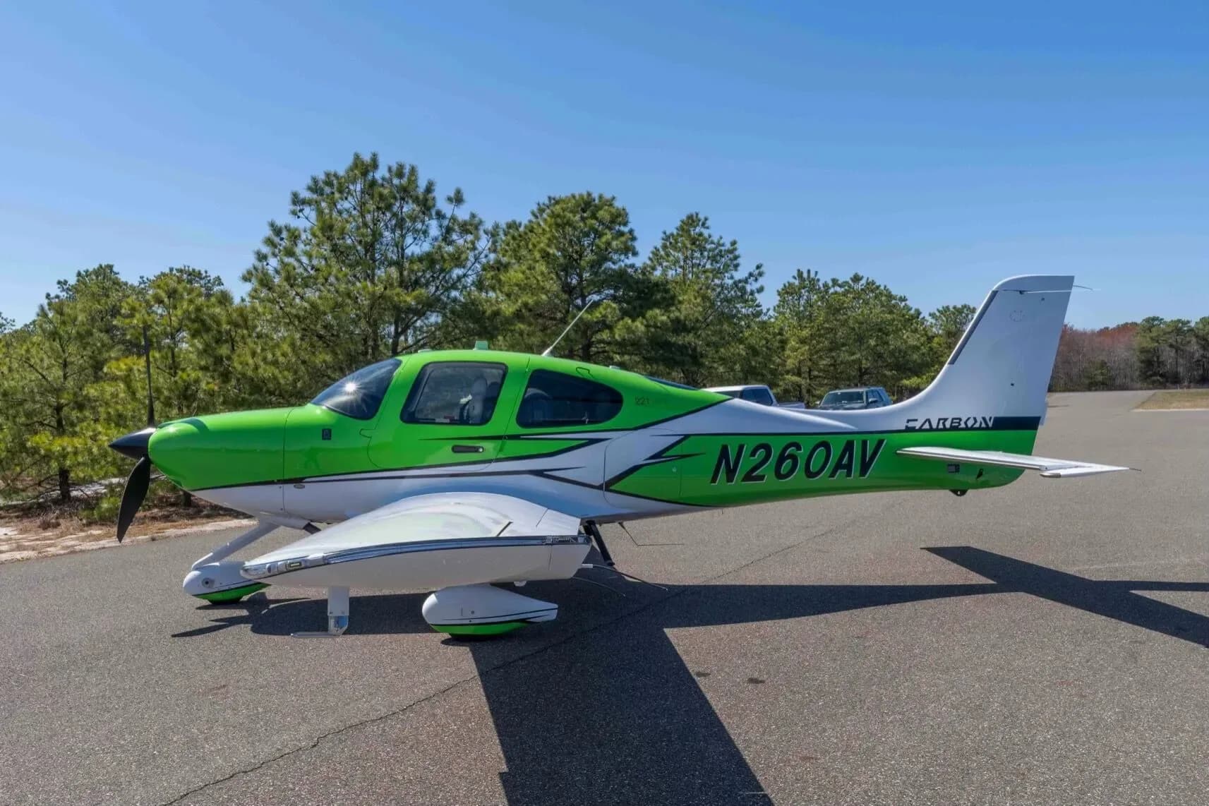 A bright green and white Cirrus SR22T aircraft, registration N260AV, parked on an asphalt ramp with trees in the background.