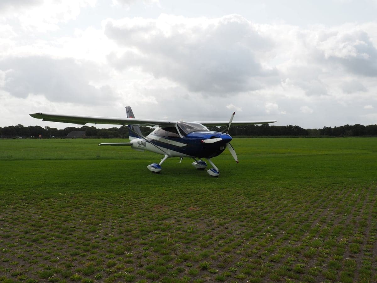 A blue and white light aircraft, registration PH-THW, sits on a grassy field.