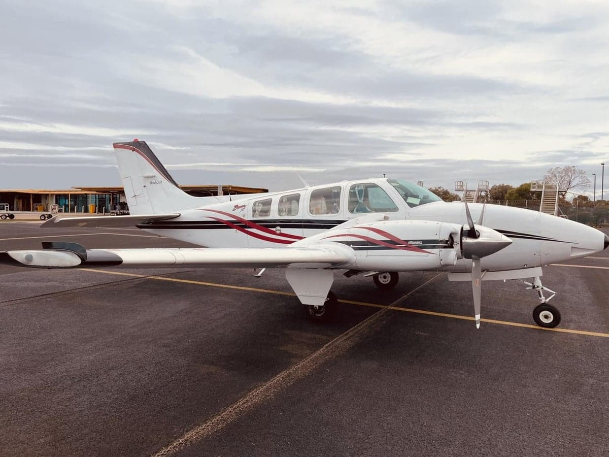 A Beechcraft Baron sits on the tarmac with a white and red paint scheme.
