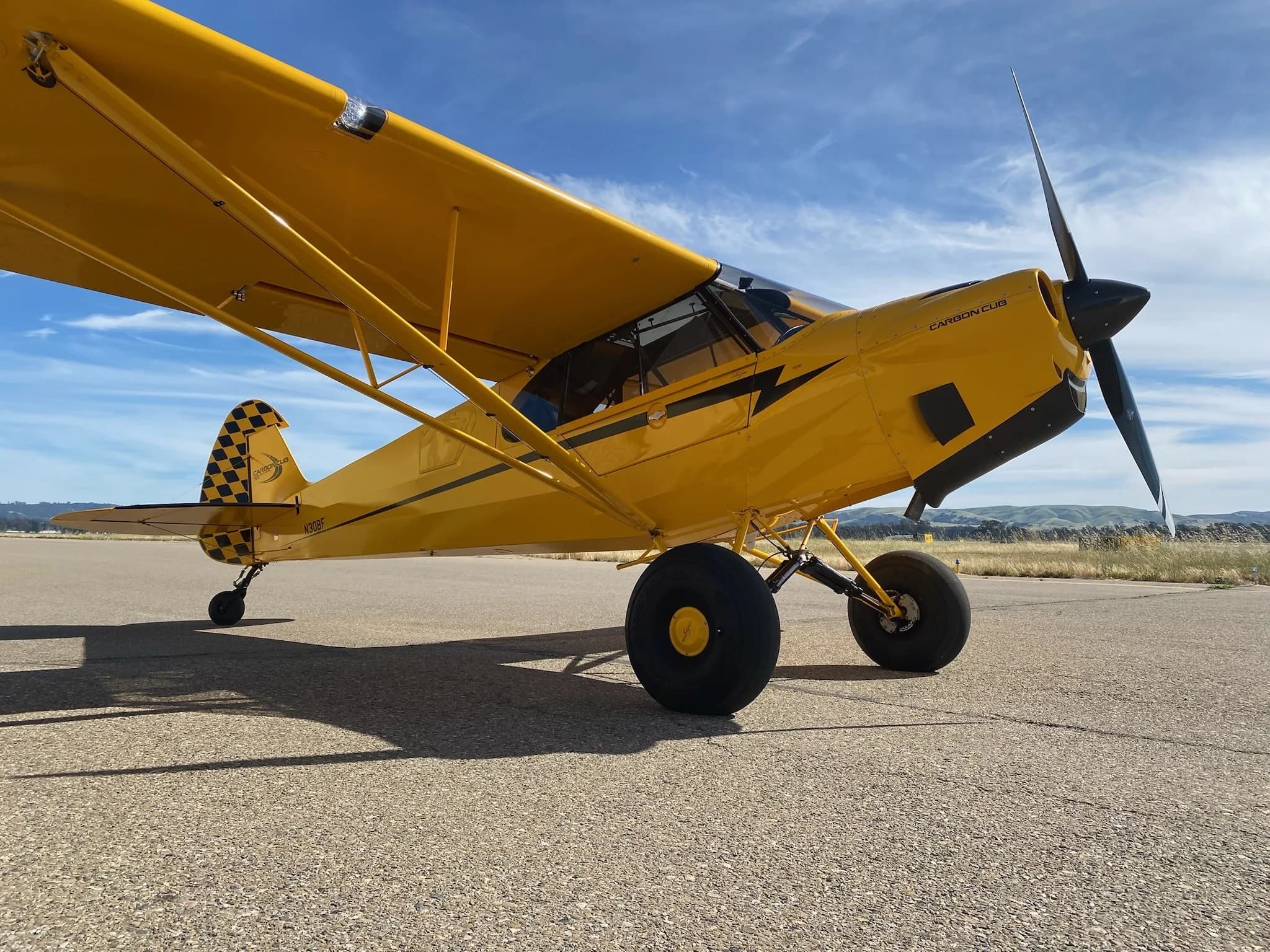 A yellow Carbon Cub aircraft is parked on the tarmac under a blue sky.