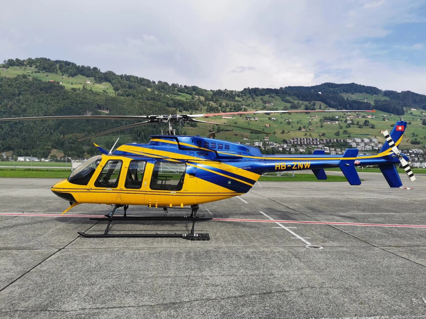 A yellow and blue Bell 505 helicopter is parked on the tarmac.