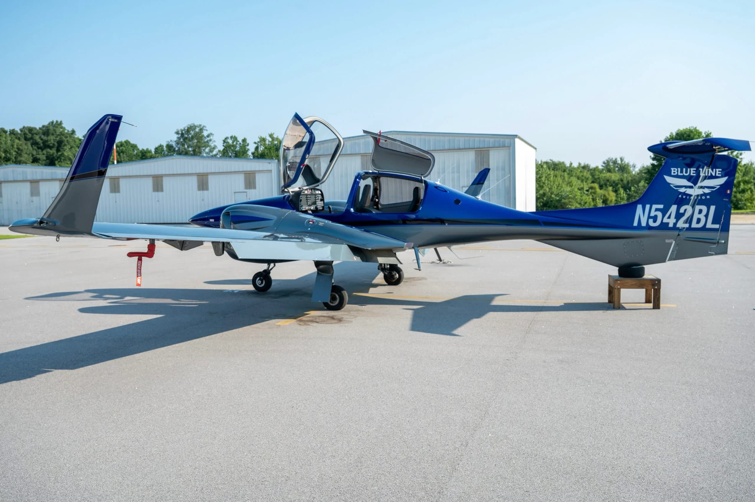 A blue and grey Diamond DA42 aircraft with doors open, parked on an airfield.