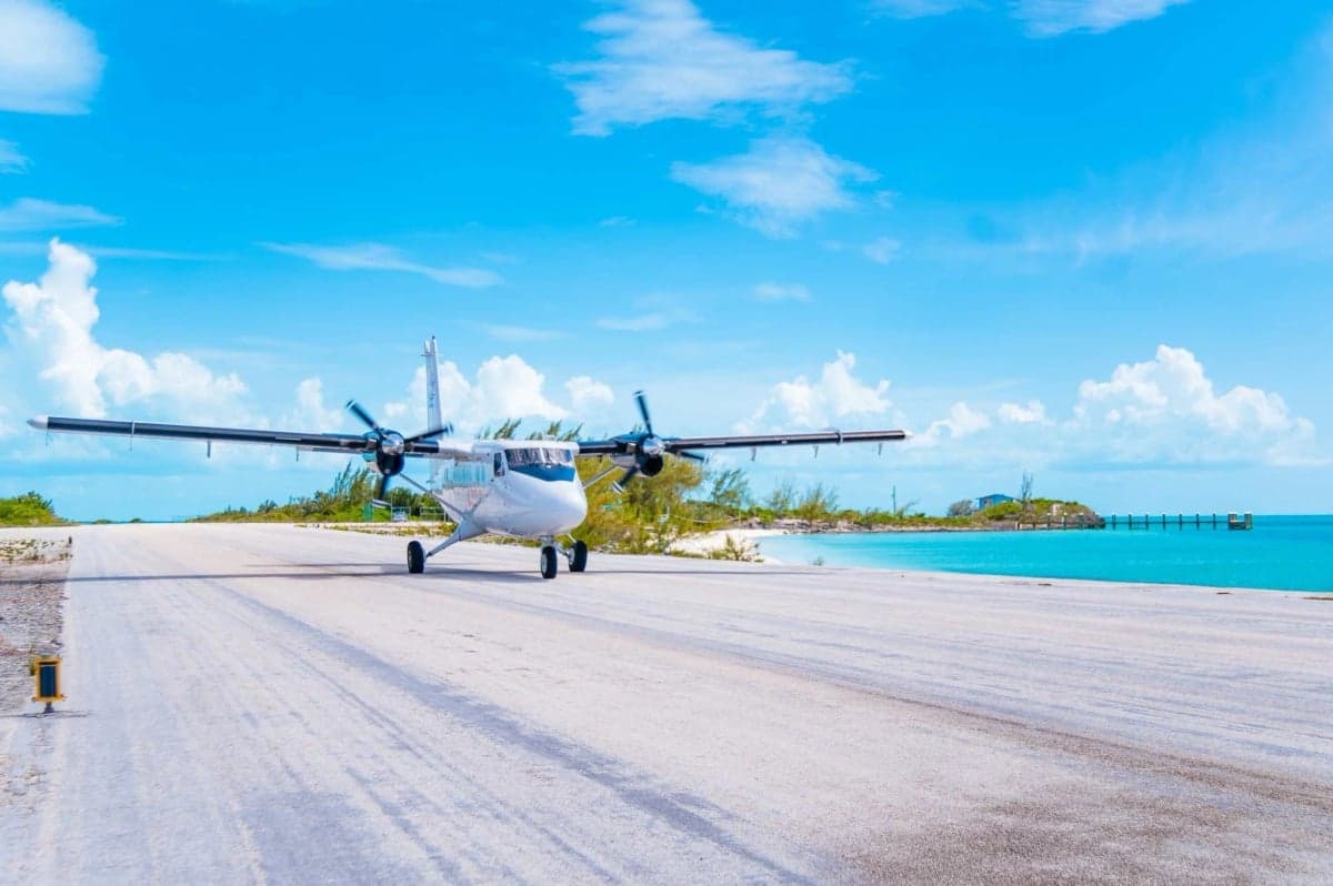 A Twin Otter aircraft on a runway near a tropical beach.