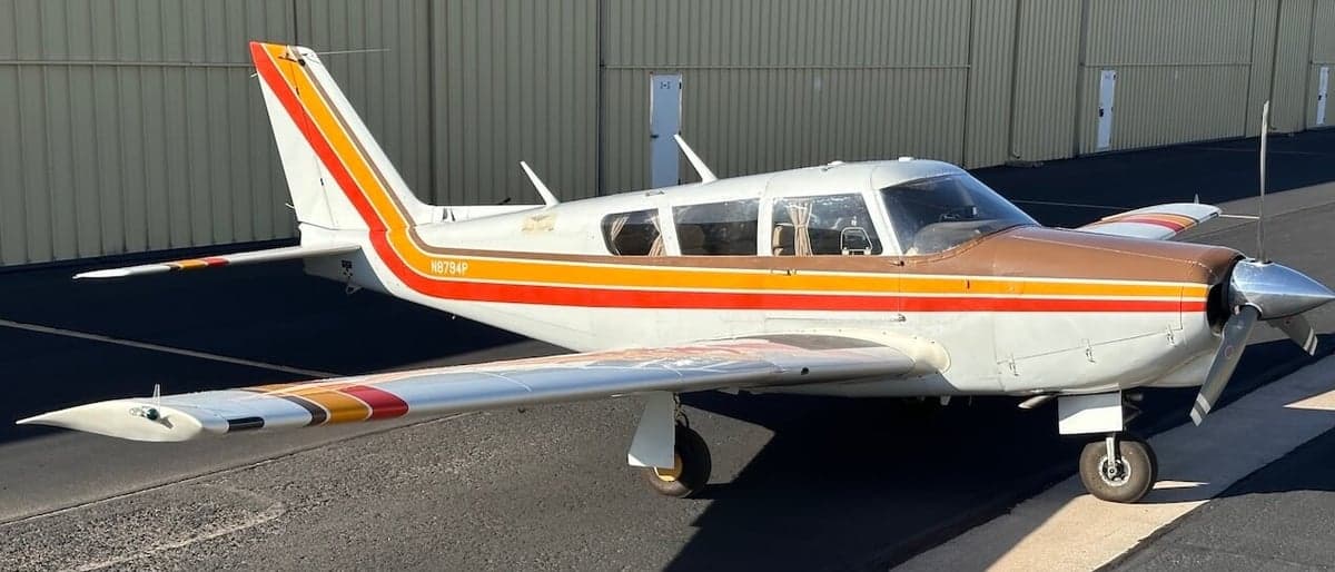 Side view of a Piper PA-28-181 Archer II aircraft with a white, brown, orange, and yellow paint scheme.