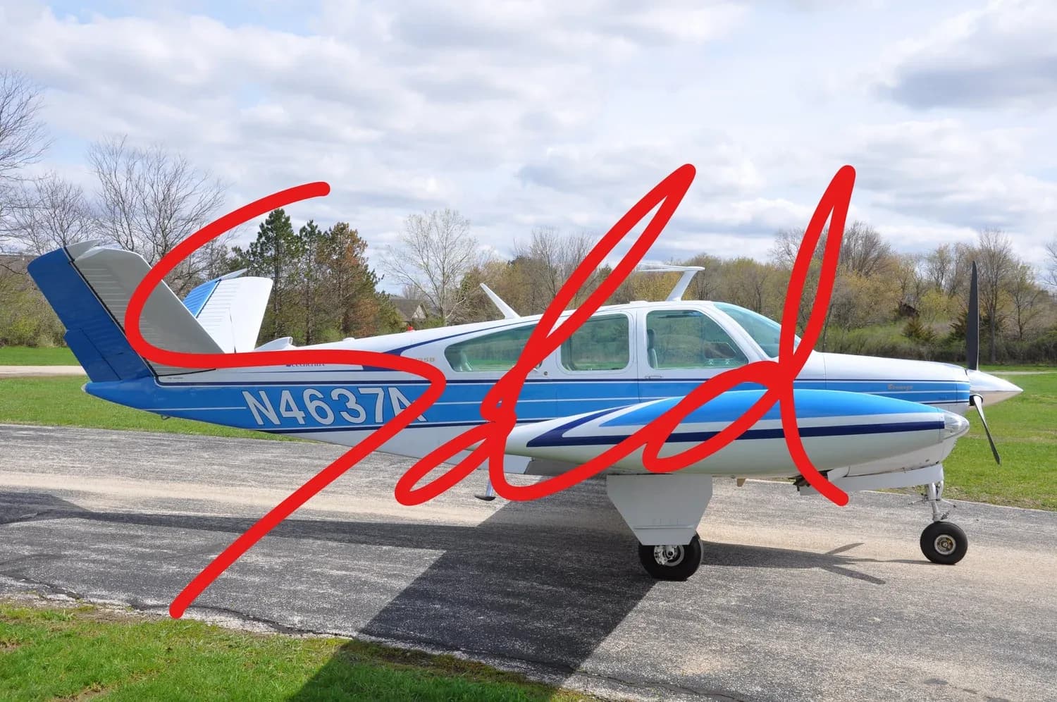 A white and blue Beechcraft Bonanza with registration N4637A, viewed from the side, parked on an asphalt runway under a partly cloudy sky.