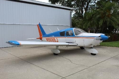 Side view of a blue and white Piper Archer aircraft with tail number N9699J parked on a concrete surface.