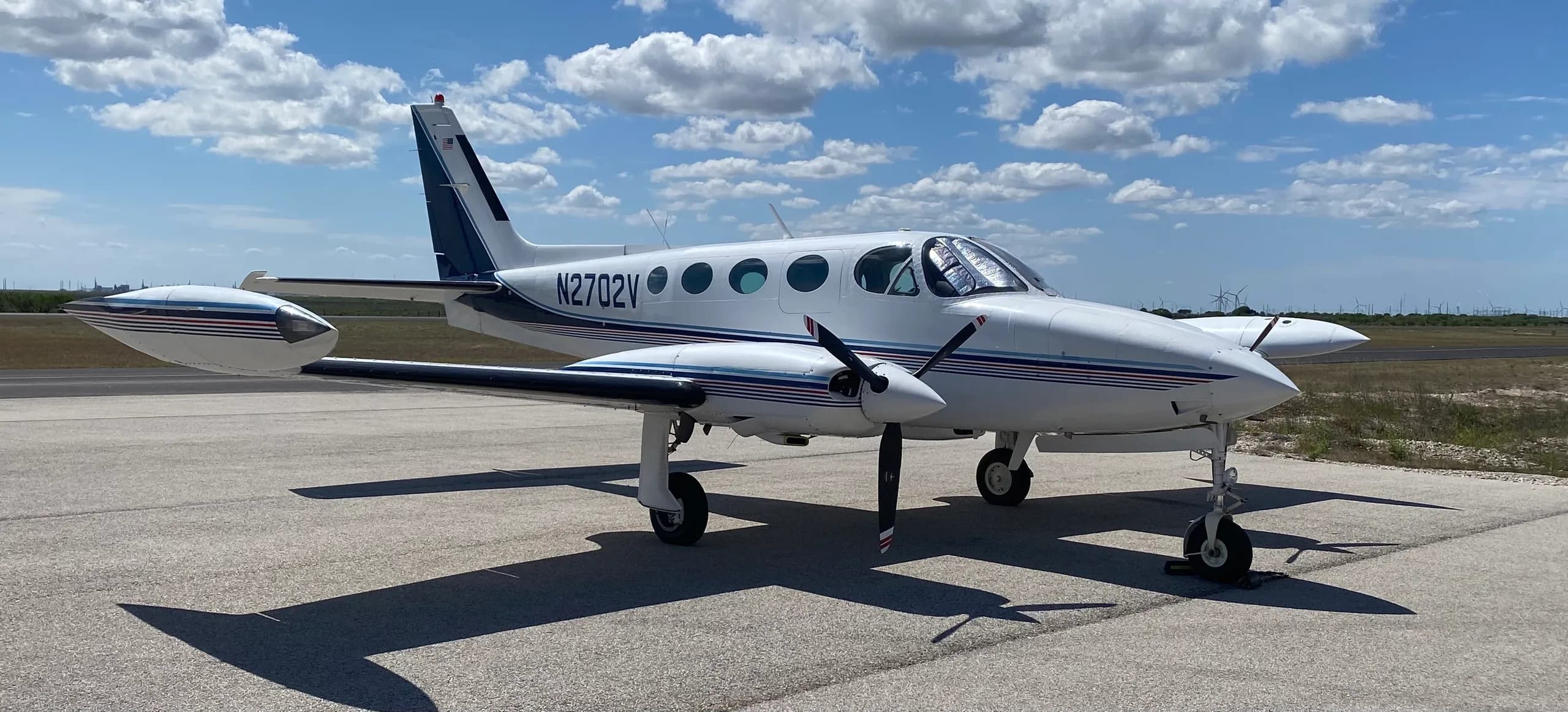 A Cessna 340A aircraft with registration N2702V parked on the tarmac under a blue sky.