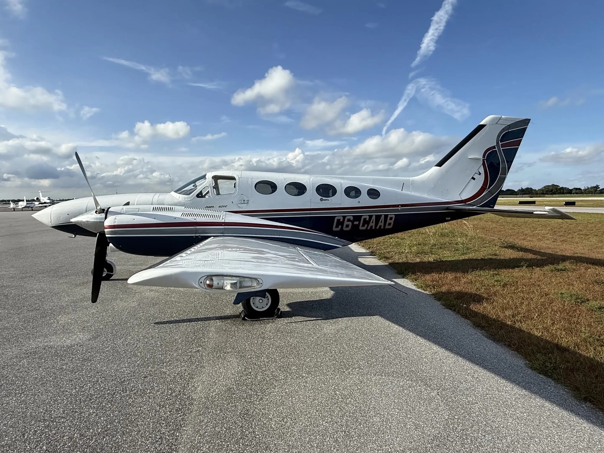 A white and blue Cessna 414 Chancellor twin-engine aircraft with registration C6-CAAB parked on an asphalt tarmac under a blue sky.