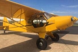 A yellow Piper Cub aircraft is parked on the tarmac.
