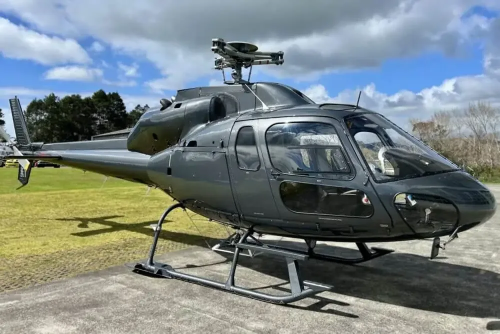 A dark grey Eurocopter AS355 F1 helicopter parked on a concrete pad under a partly cloudy sky.