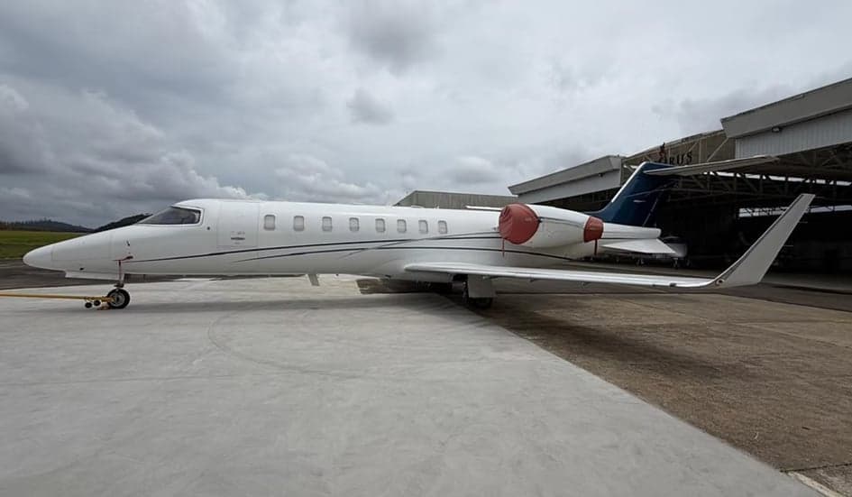 Side view of a white Learjet on the tarmac in front of a hangar.