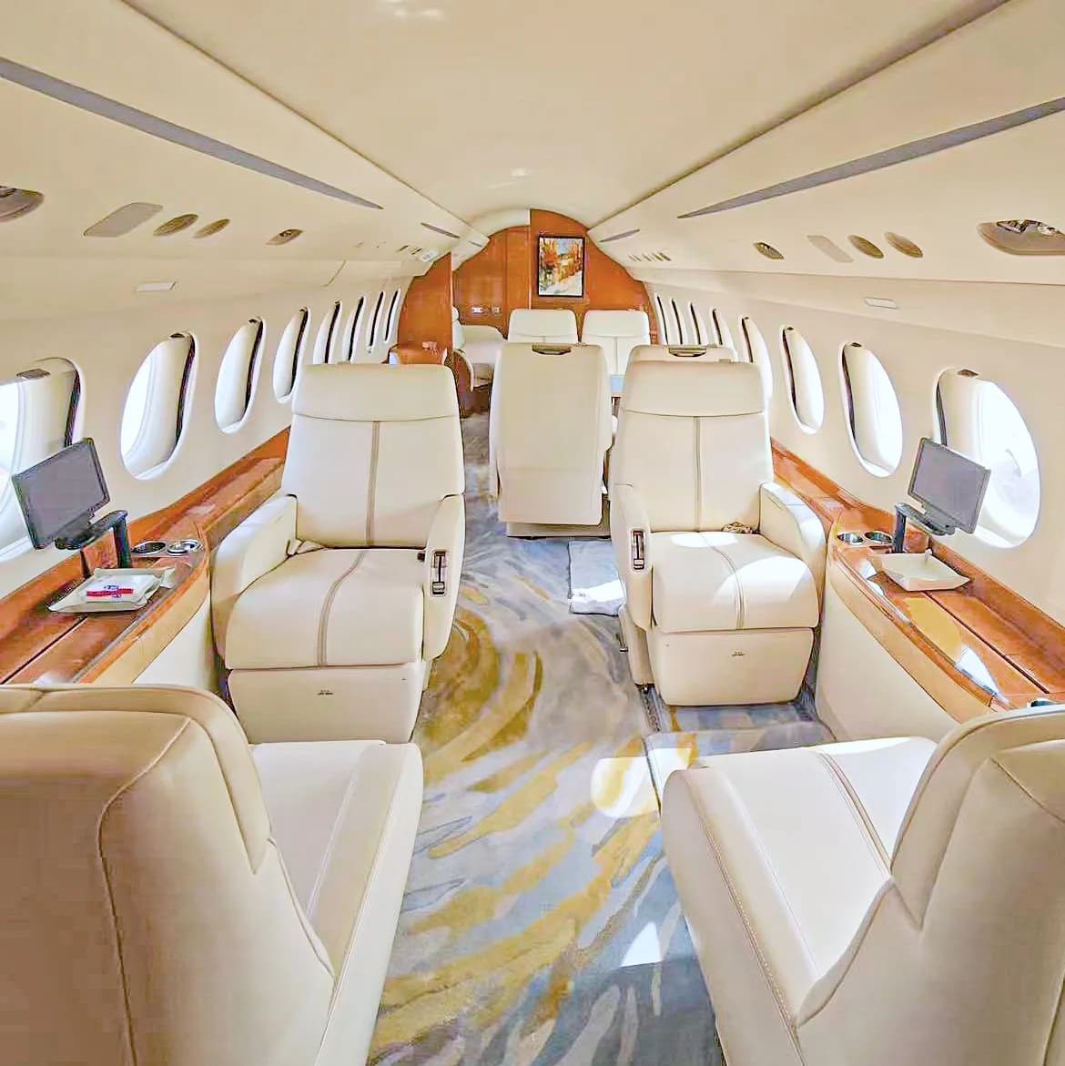 A luxurious private jet interior with cream leather seats, wood paneling, and a colorful patterned carpet.