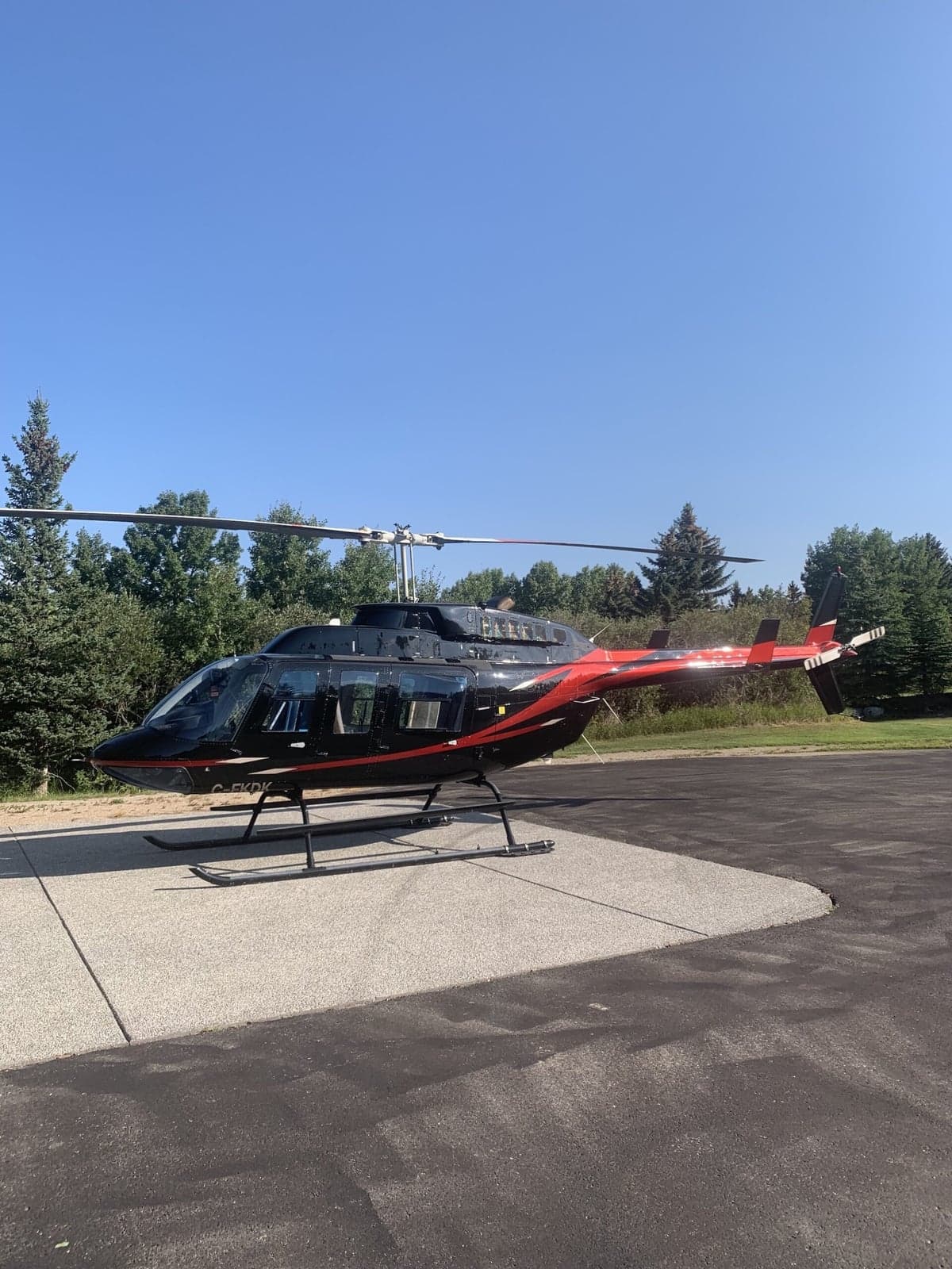 A black and red Bell 407 helicopter is parked on a concrete pad.