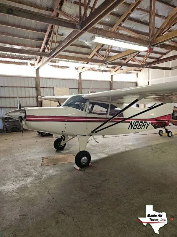 A white single-engine, high-wing aircraft with red stripes and registration N88BRV, parked in a hangar.