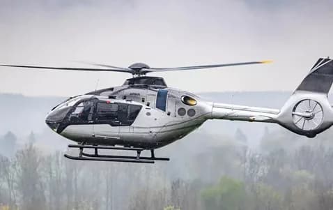 A silver Airbus H145 helicopter in flight against a cloudy sky.