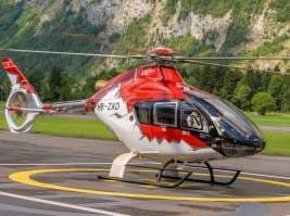 A red and white Airbus H135 helicopter on the ground.