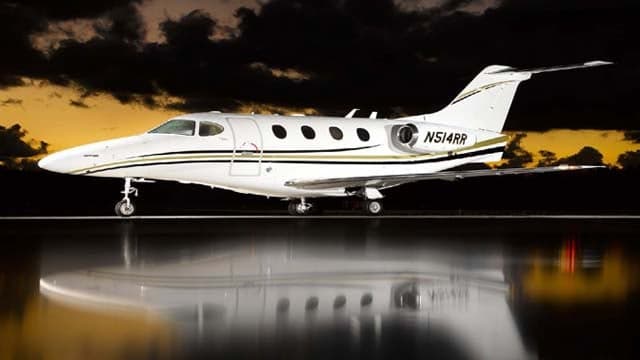 A Citation CJ3+ aircraft with registration N514RR is parked on a reflective surface at sunset.