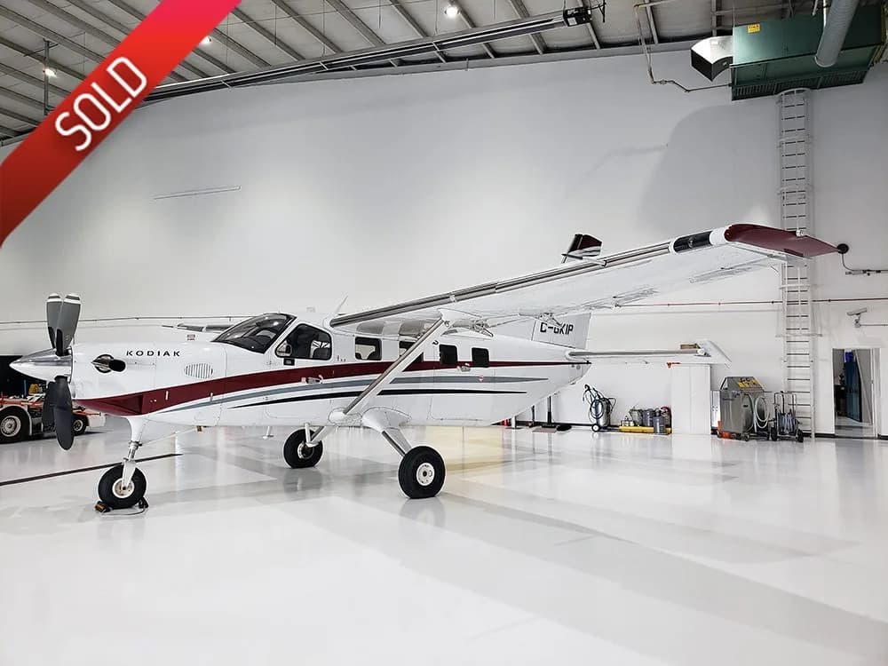 A white and maroon Kodiak aircraft with registration C-GKIF is parked inside a brightly lit hangar.