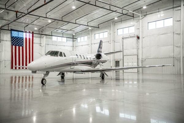A Citation jet, N338HR, is parked in a hangar with an American flag in the background.