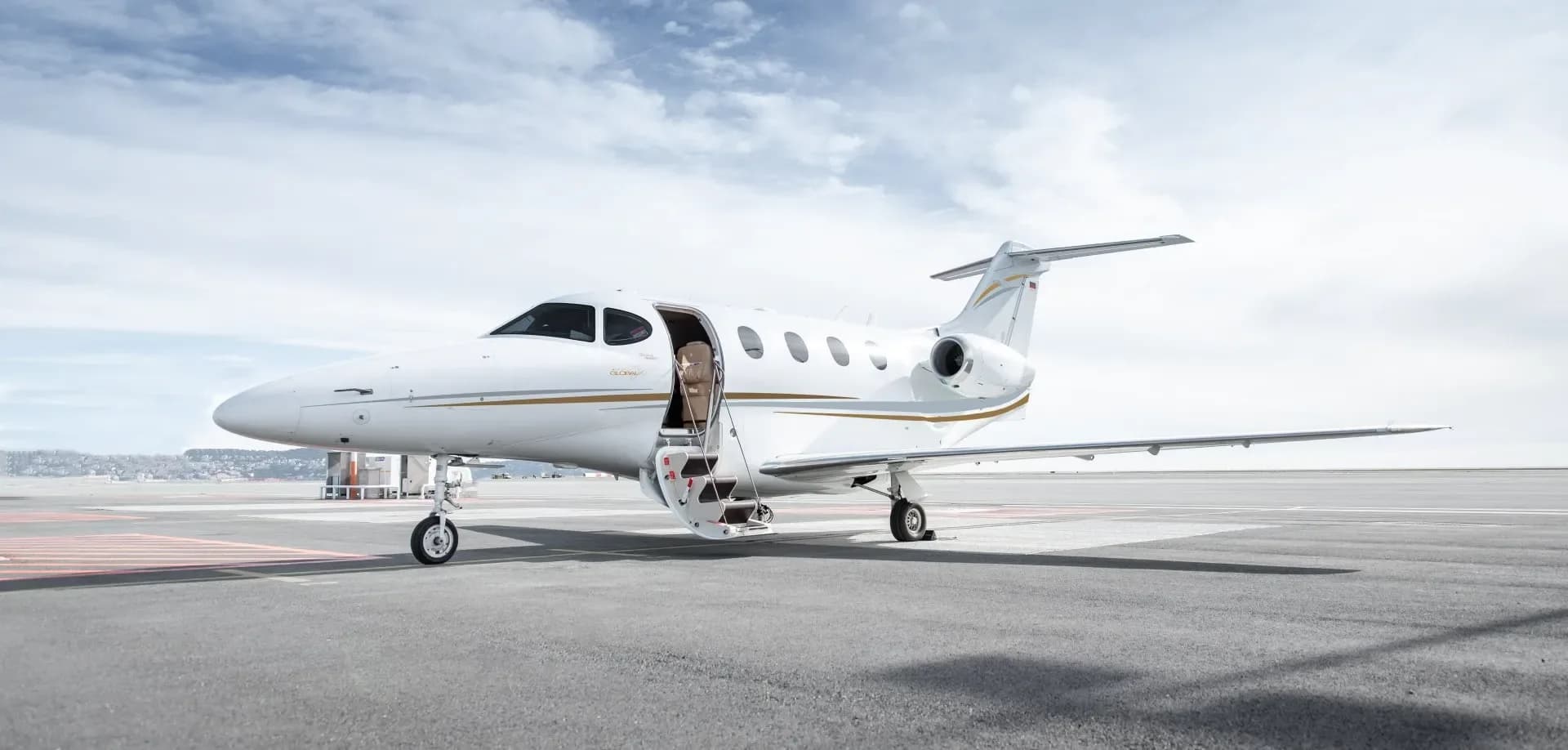 A white jet with gold trim sits on the tarmac with its door open.