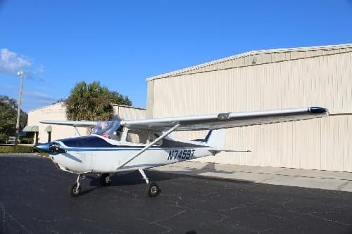 Cessna 150 aircraft N7459T parked on the tarmac in front of a hangar.